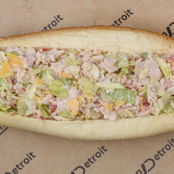 A close-up, top-down view of a sub sandwich filled with chopped ham, lettuce, cheese, and dressing.