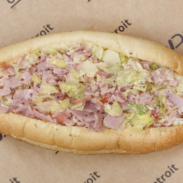 Close-up of a sub sandwich filled with chopped ham, lettuce, and cheese on a brown paper background.