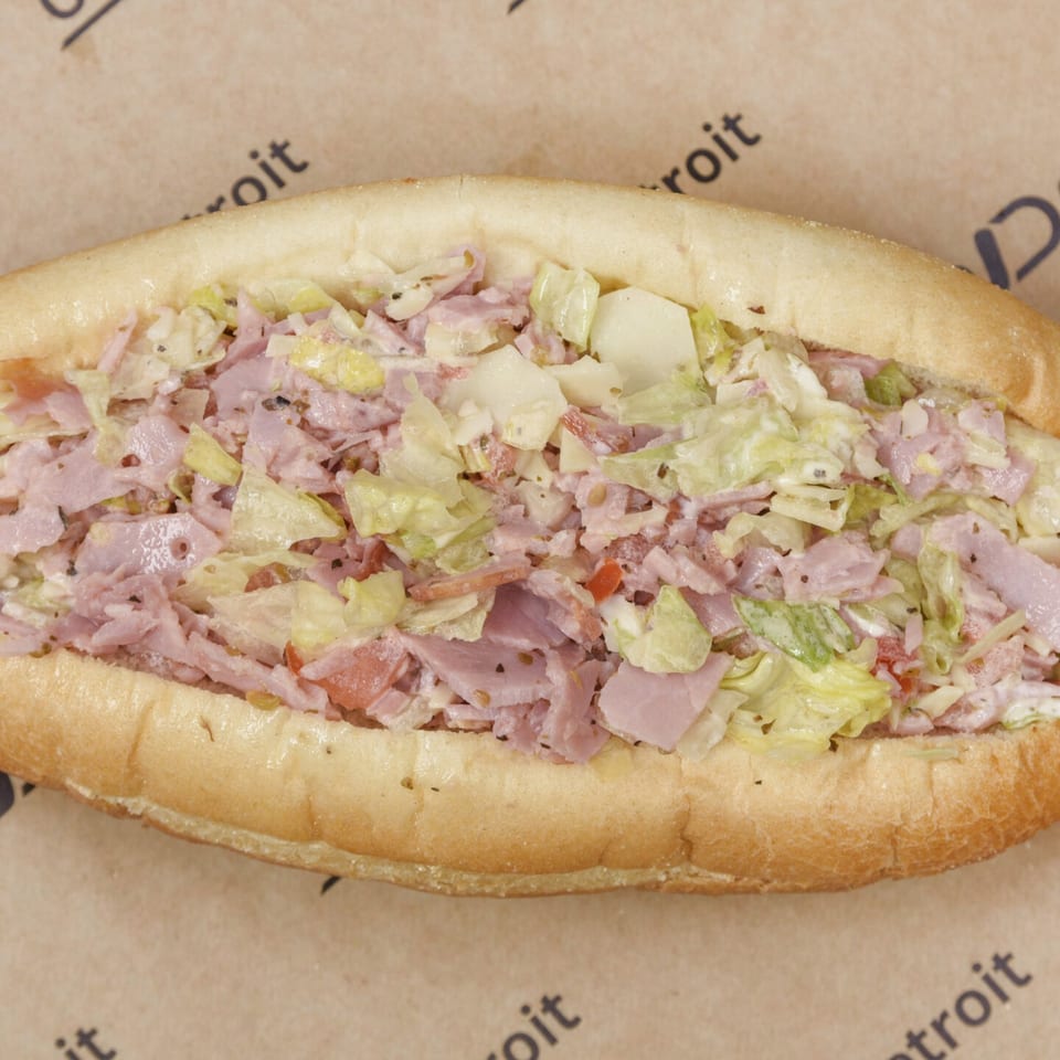 Close-up of a sub sandwich filled with chopped ham, lettuce, and cheese on a brown paper background.