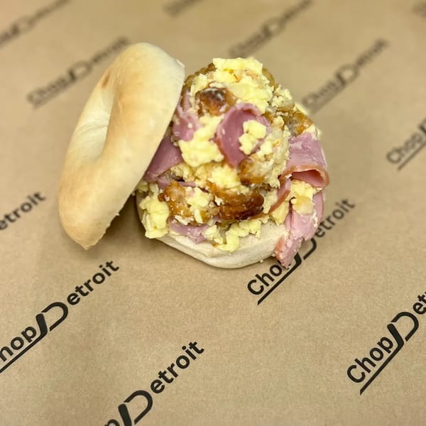 Chop Detroit's bagel sandwich with scrambled eggs, ham, and crispy hash browns on branded paper.