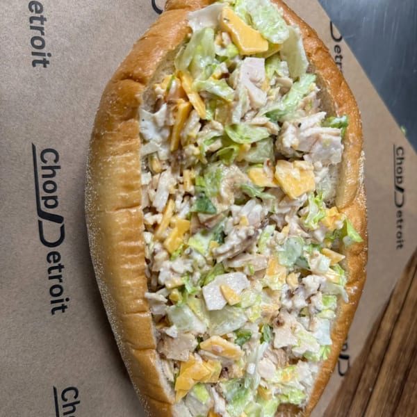 A Chop Detroit chicken salad sandwich with lettuce and cheese on a brown paper background.